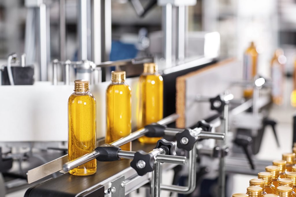 Factory  and research concept. Bottles with yellow thick substance standing on manufacturing facility going to be twisted. Glass bottles in line on conveyor belt. Production process of cosmetics